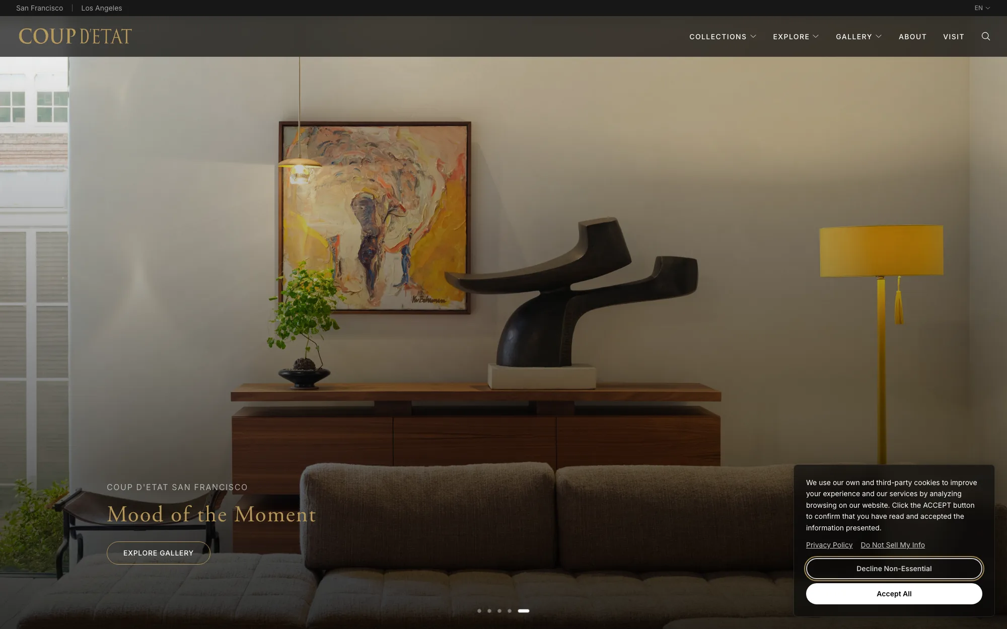 The Coup D’Etat homepage: a photographed interior in warm afternoon light — a sculptural black side table, a yellow floor lamp and an abstract painting above a walnut credenza — with the caption “Mood of the Moment” and an “Explore Gallery” button. A cookie consent panel sits over the lower right corner.