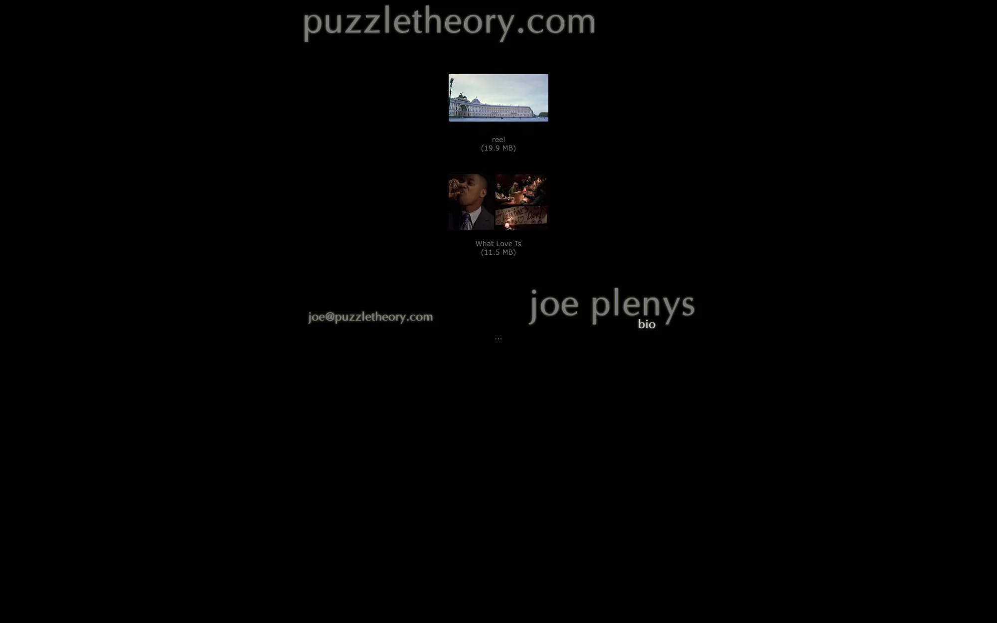 The puzzletheory.com homepage: an almost entirely black page with the domain set large in grey at the top, two small video thumbnails labelled “reel” and “What Love Is” with their file sizes, and a contact address beside the name “joe plenys”.